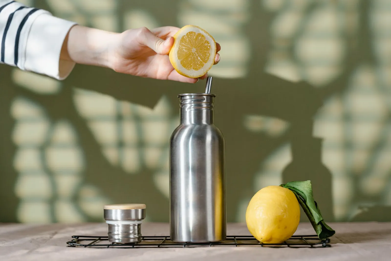 A hand squeezing fresh lemon over a stainless steel refill bottle